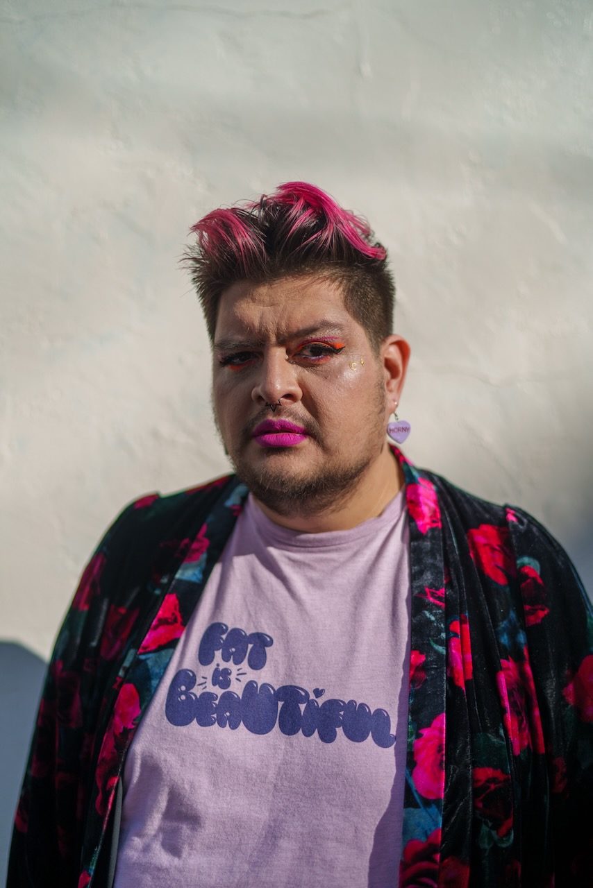 Straight-on portrait of Violet Paniko with pink hair and a floral jacket against a white wall